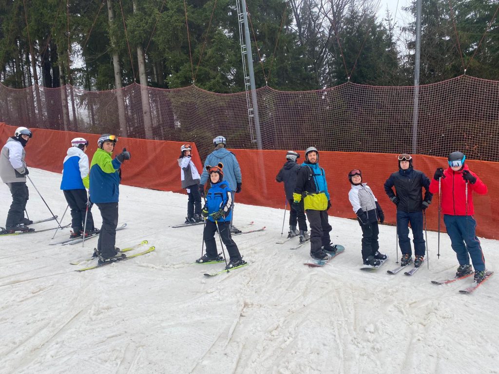 9.	Společná fotka školní skupiny 11 žáků a jednoho učitele fotící se na okraji sjezdovky ve skiareálu Špičák.