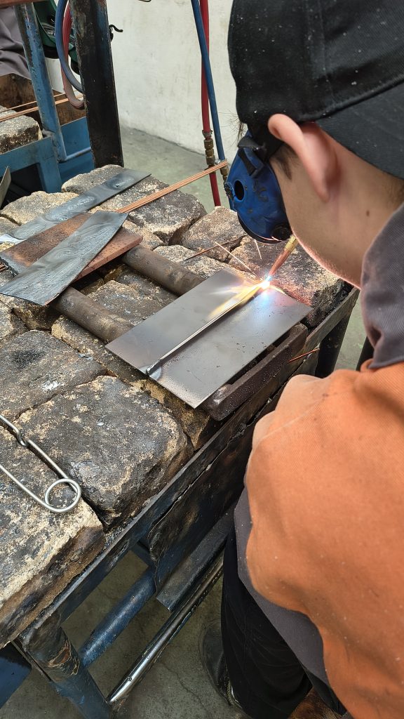 Pohled přes rameno žáka, jak svařuje plamenem