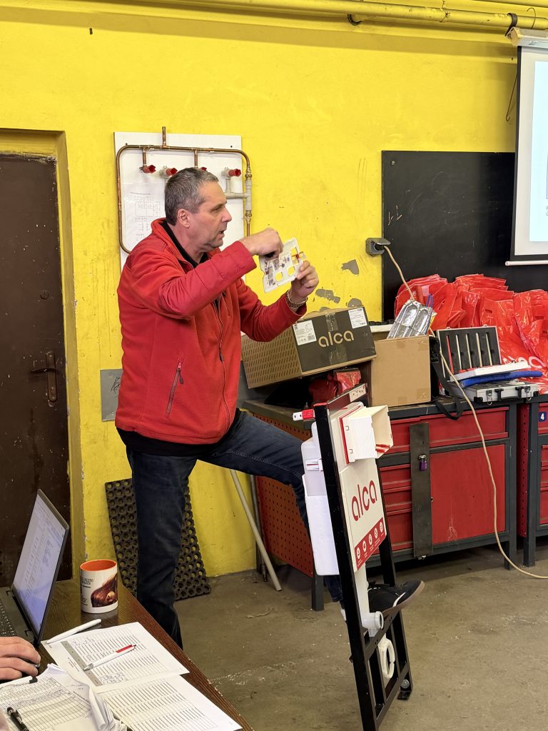 Odborný školitel společnosti ALCA vede výklad přímo v dílnách školy před žáky 1. a 3. ročníků (třídy 1.C a 3.C). Součástí prezentace je vysvětlení správných montážních a servisních postupů a seznámení s moderními instalačními systémy používanými v současné stavební praxi.