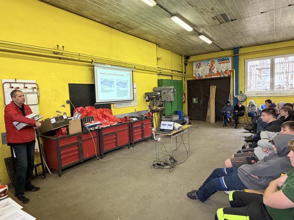 Celkový pohled na odborné školení realizované přímo ve školní dílně. Žáci mají možnost vidět produkty ALCA v reálném měřítku, klást dotazy a získat informace, které jim pomohou při budoucím uplatnění v oboru. Takové propojení výuky s praxí přináší studentům cenné zkušenosti a jasnou představu o jejich budoucí profesi.