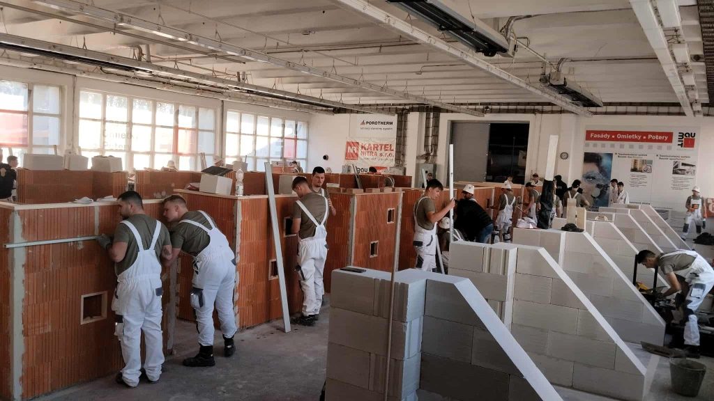 Na fotografii jsou žáci při soutěži v odborném výcviku, kde připravují a provádějí zakládání zdiva pomocí maltového lože a měřicích pomůcek.