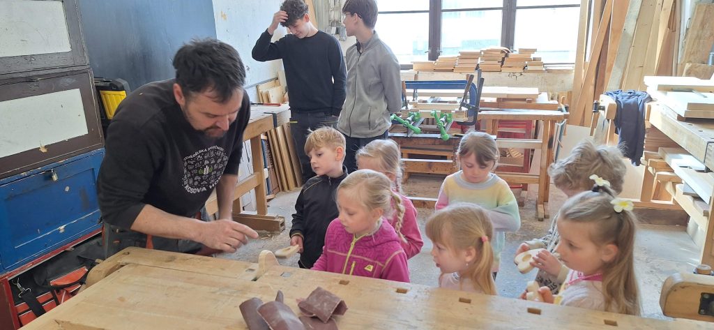 Učitel ukazuje dětem, jak se brousí dřevo.
