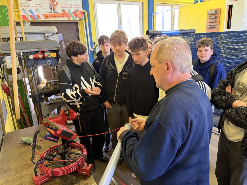 Učitel odborného výcviku jim představuje inspekční kameru, se kterou je možné nahlédnout do odpadního potrubí.